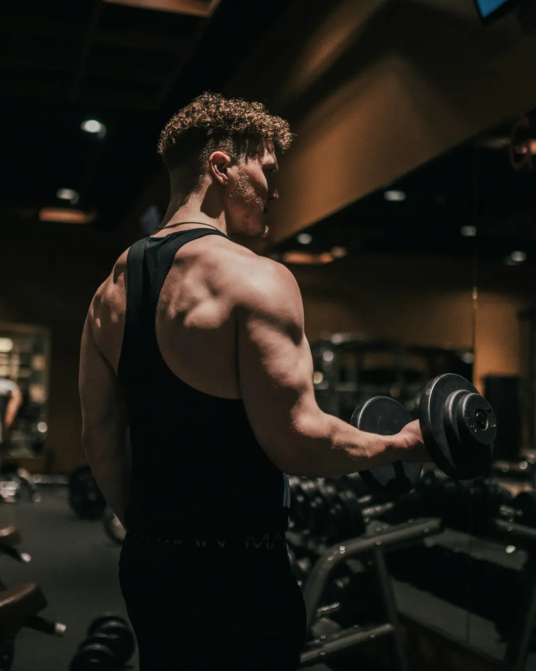 An athlete training with a dumbbell in a dark, modern gym